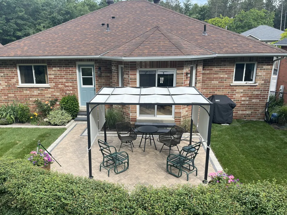 Interlocking paver patio with a gazebo-covered dining set behind a brick bungalow in Barrie, ON
