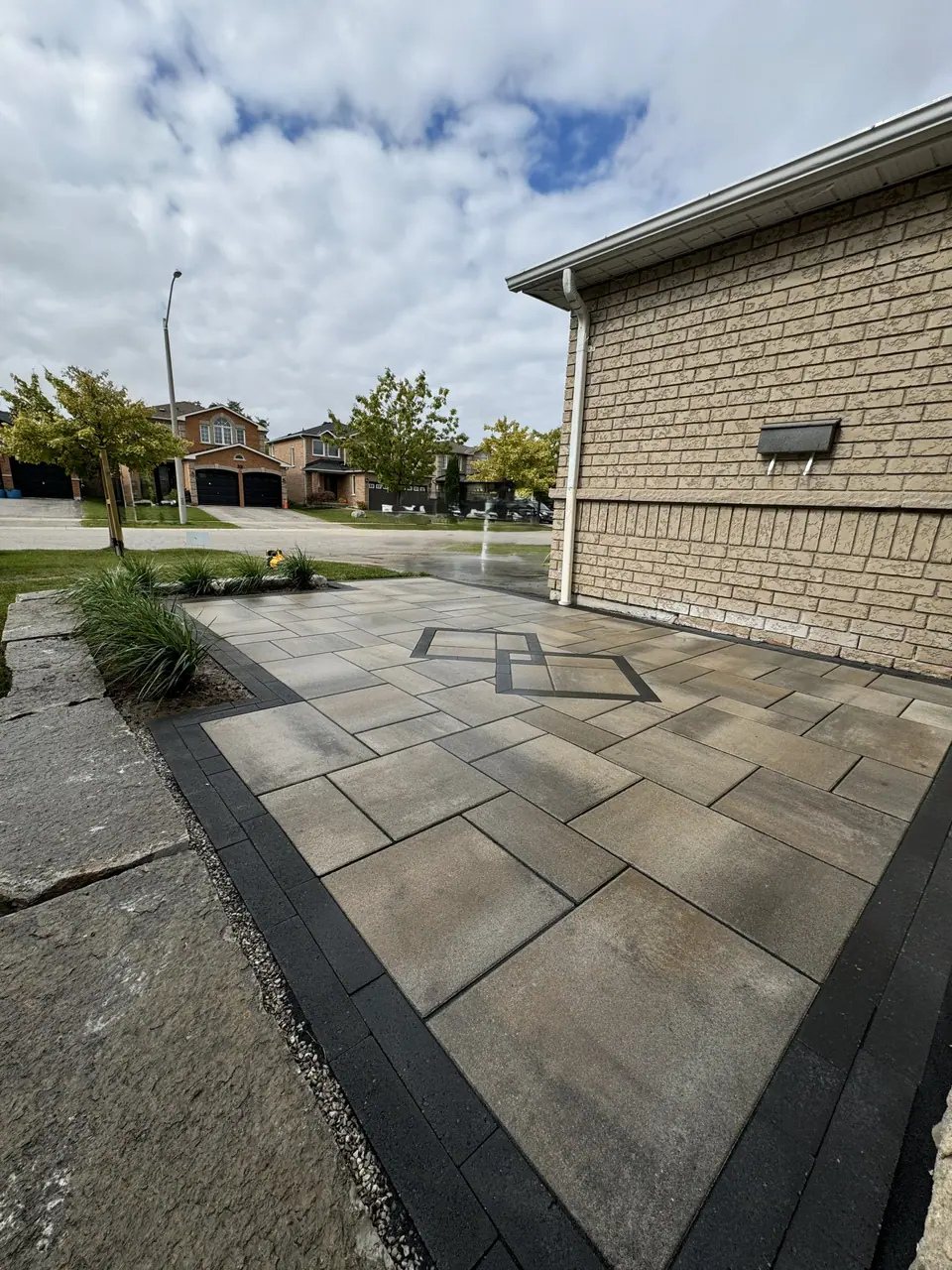 Slab patio with a dark border and a diamond inlay beside a brick home in Simcoe County, ON