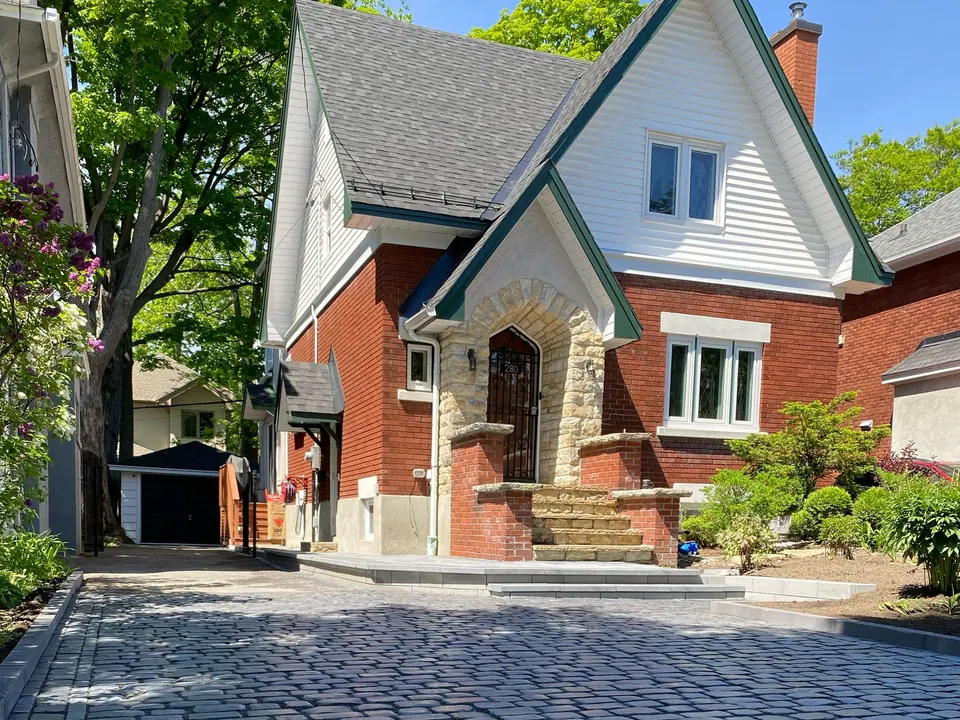 Cobblestone-style paver driveway with a border leading to stone-pillar front steps of a red-brick home in Simcoe County, ON