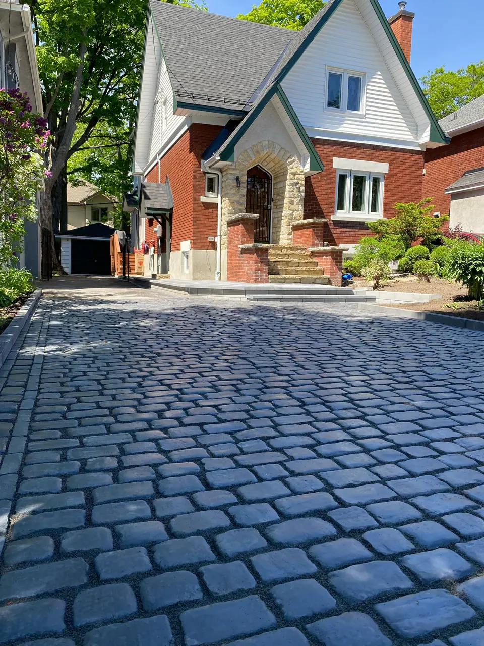 Cobblestone-style paver driveway with a border leading to stone-pillar front steps of a red-brick home in Simcoe County, ON