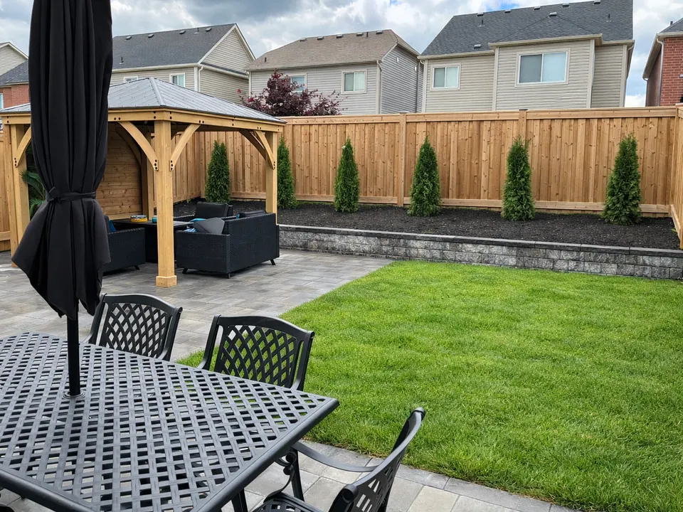 Slab patio with a cedar gazebo over a dining set, a low block wall and a new lawn in Simcoe County, ON