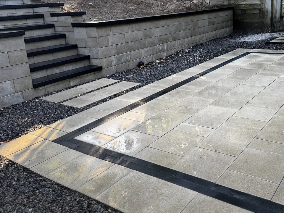 Block retaining wall with built-in steps down to a slab patio with a charcoal border in Simcoe County, ON