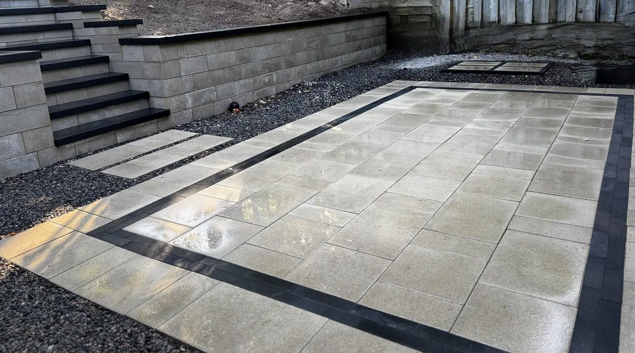 Block retaining wall with built-in steps down to a slab patio with a charcoal border in Simcoe County, ON